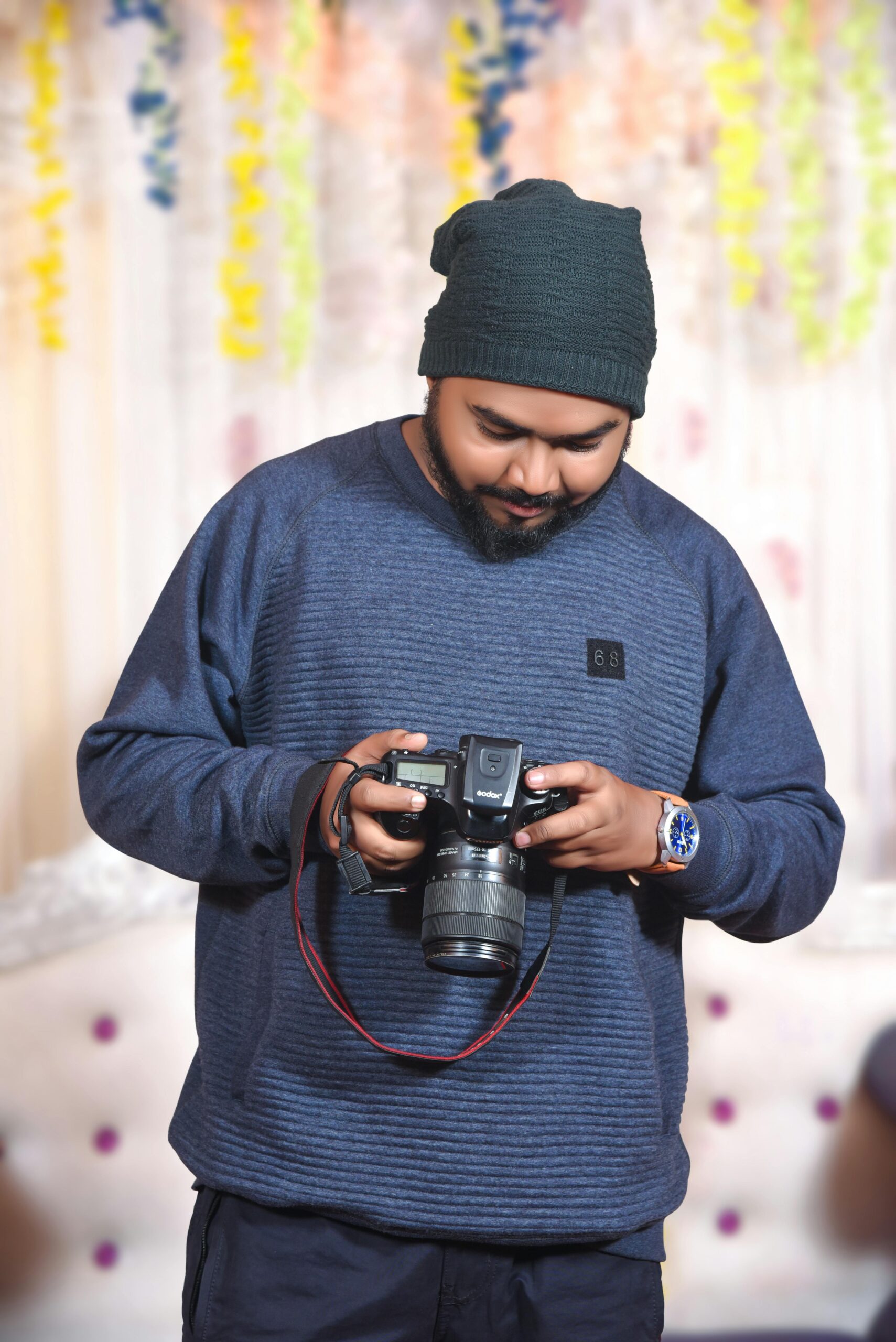 A bearded man in a beanie using a DSLR camera indoors in Jamshedpur, India.